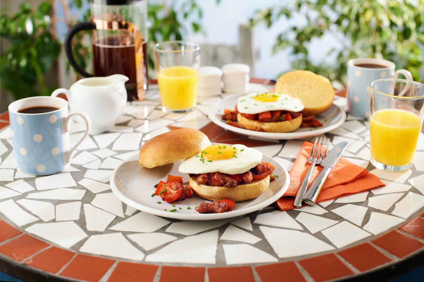 Red Pepper And Pancetta Brunch Burgers. A table with plates and breakfast burgers in an outdoor setting